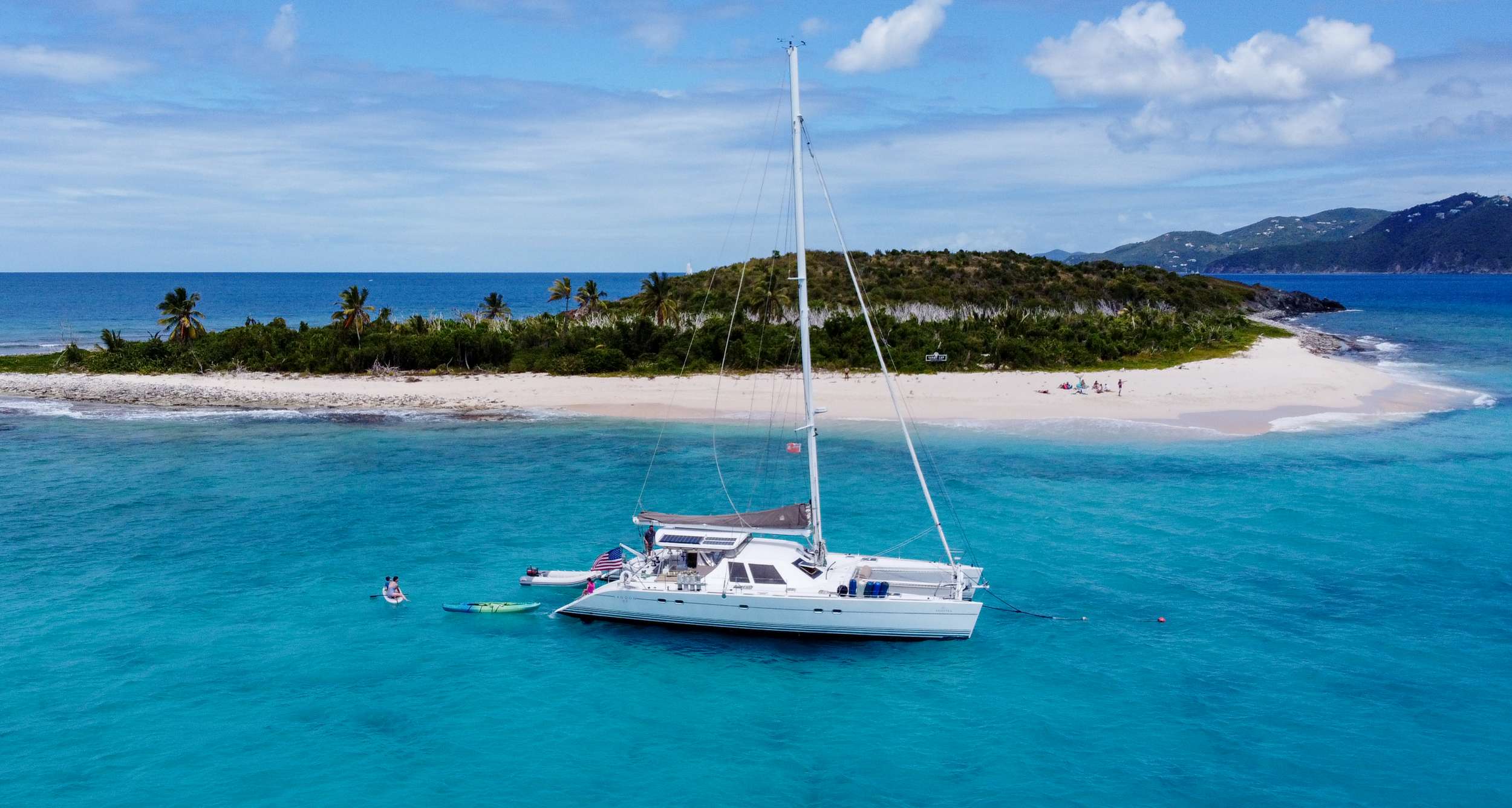 Ad Astra Lagoon 57 catamaran anchored off a secluded beach in Tortola, British Virgin Islands with turquoise waters and kayakers nearby.