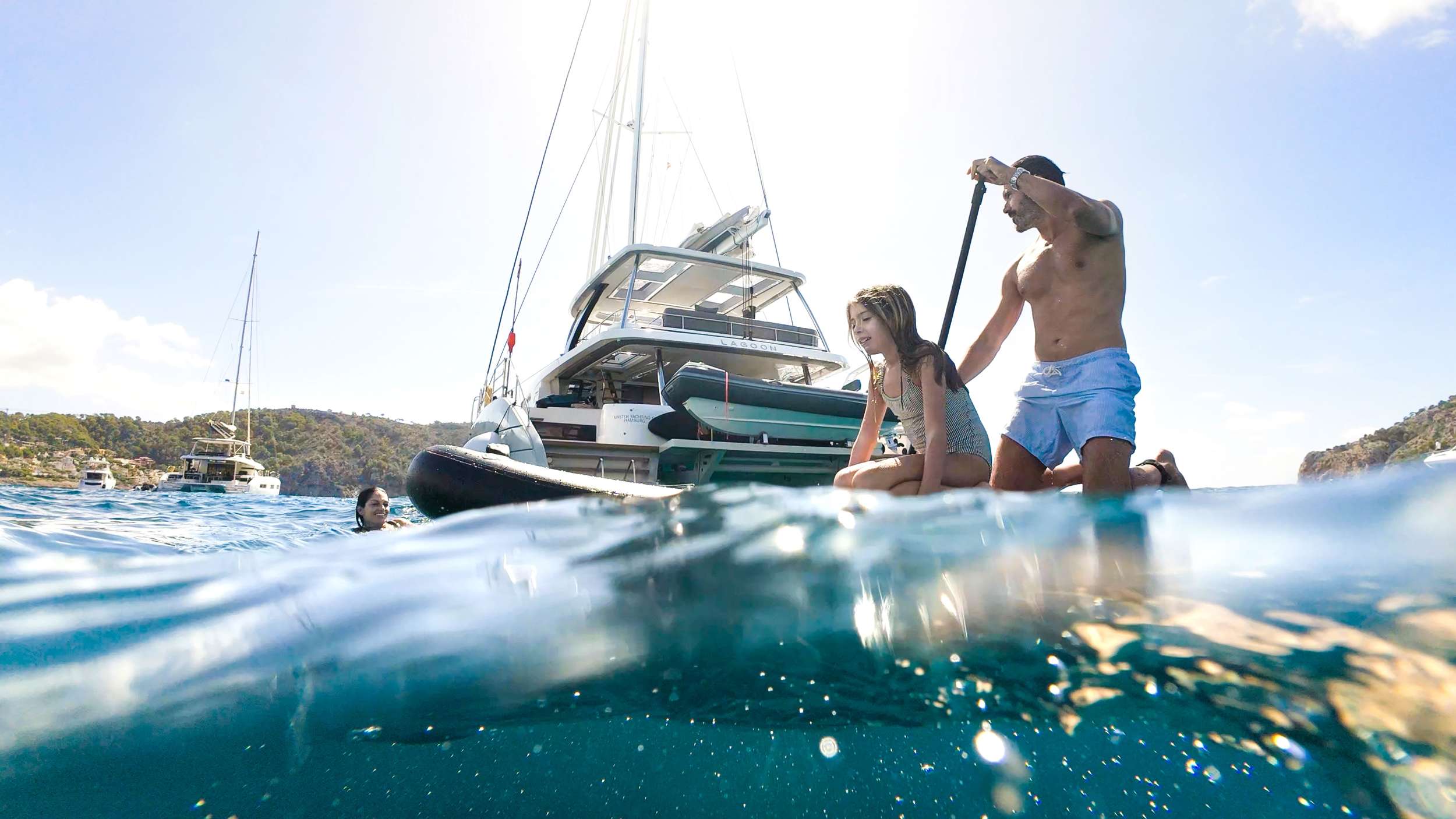 Guests enjoying paddleboarding and swimming off the luxury catamaran Triwing Endor in clear Caribbean waters, with the yacht anchored nearby during a private family yacht charter.