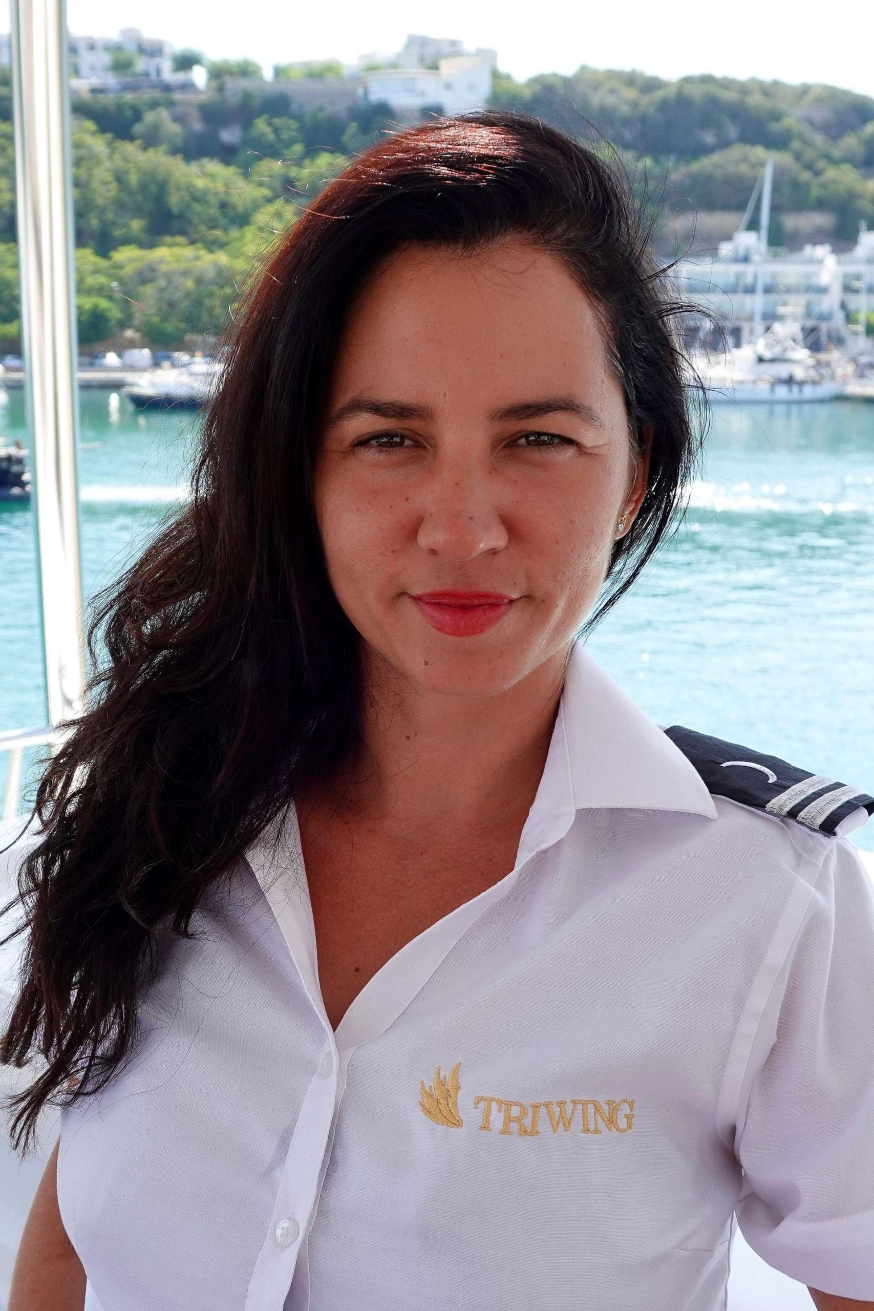 Professional hostess aboard the luxury catamaran Triwing Endor, wearing uniform with marina and turquoise water in the background during a private Caribbean yacht charter.